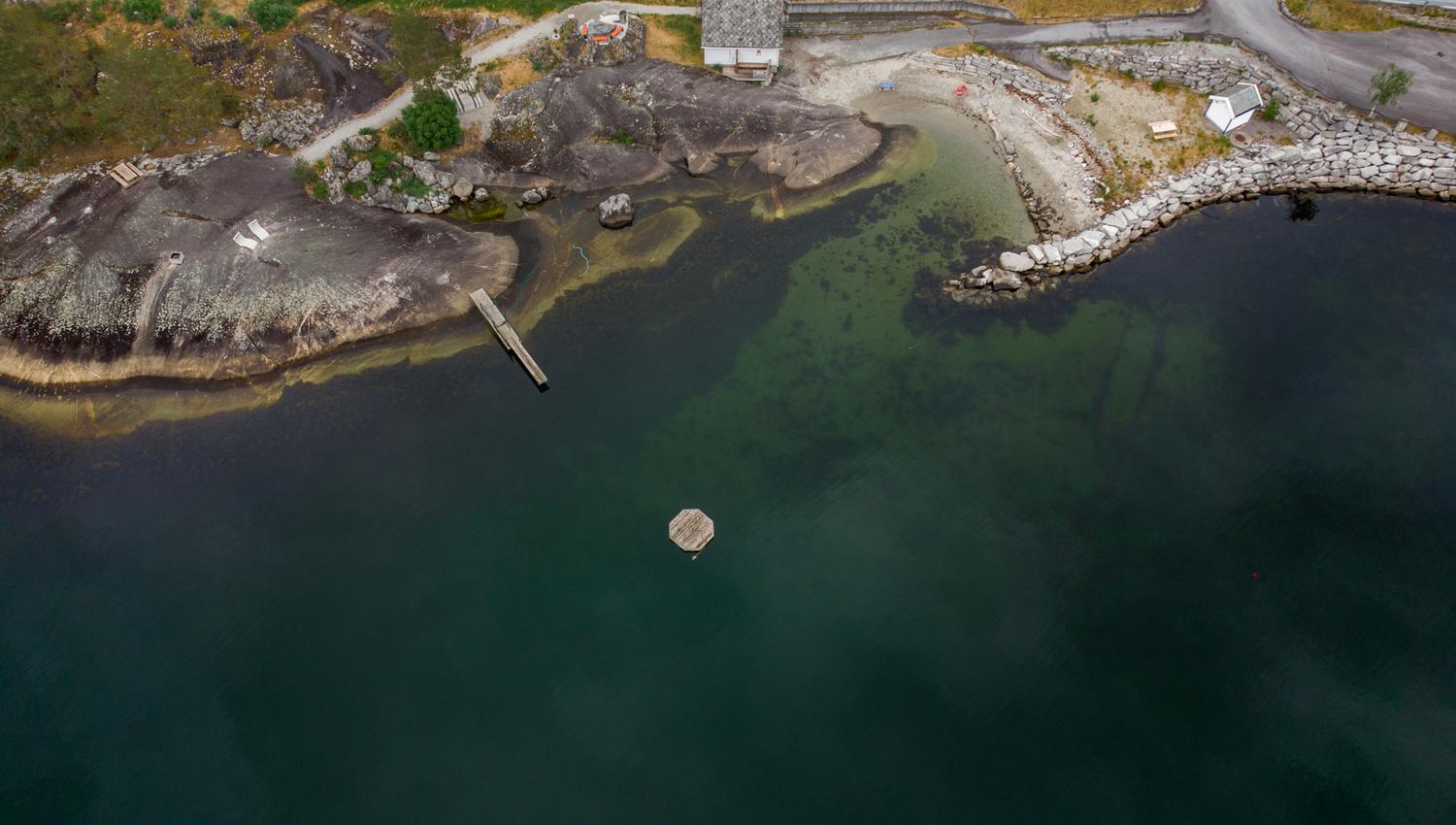 A drone shot of the Kråkeskarvet beach, showing the swim platform in the fjord, diving board, wardrobe building and the beach area.
