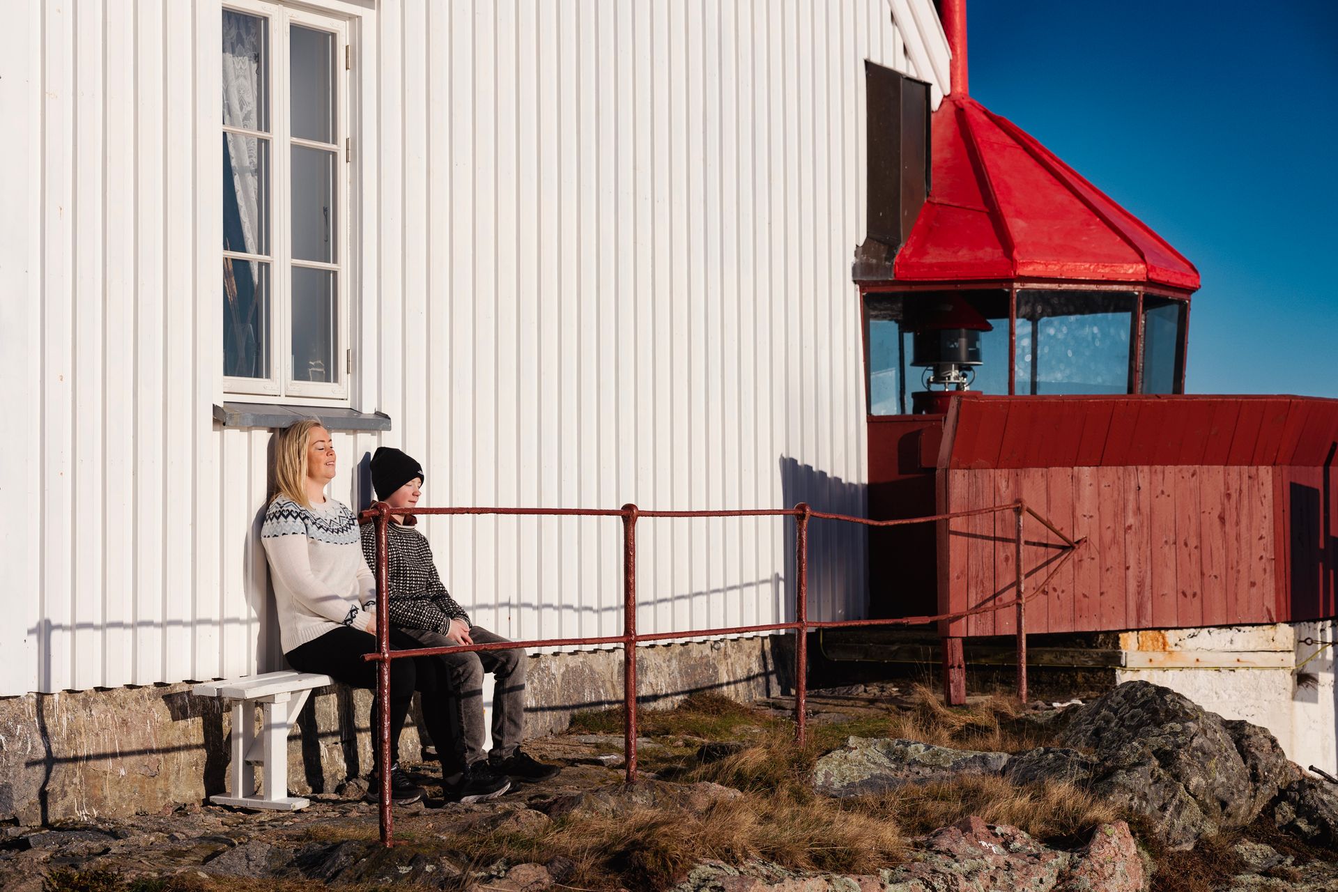 Two people sitting in the sun against the wall at Hatholmen Lighthouse