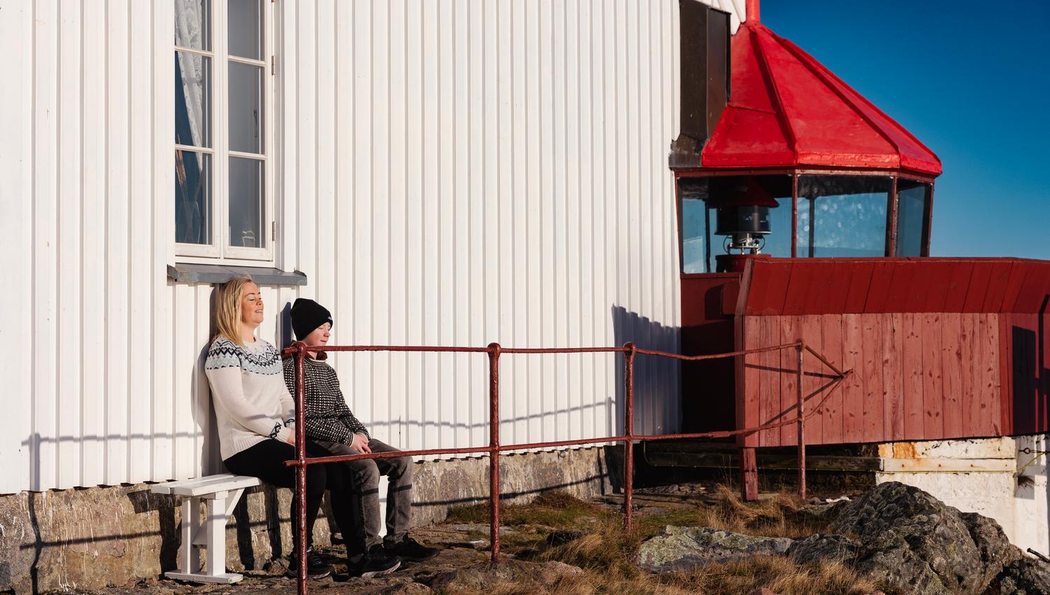 Two people sitting in the sun against the wall at Hatholmen Lighthouse