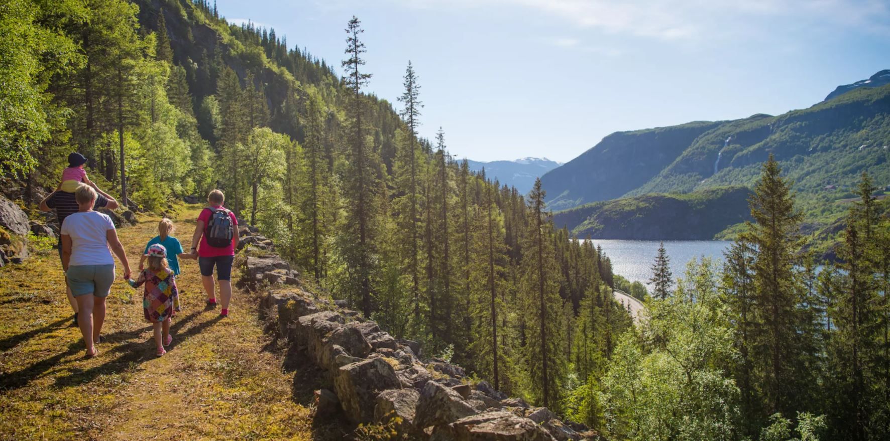 A familiy walks along a historical grass-overgrown road  in a steep hillside along a lake.