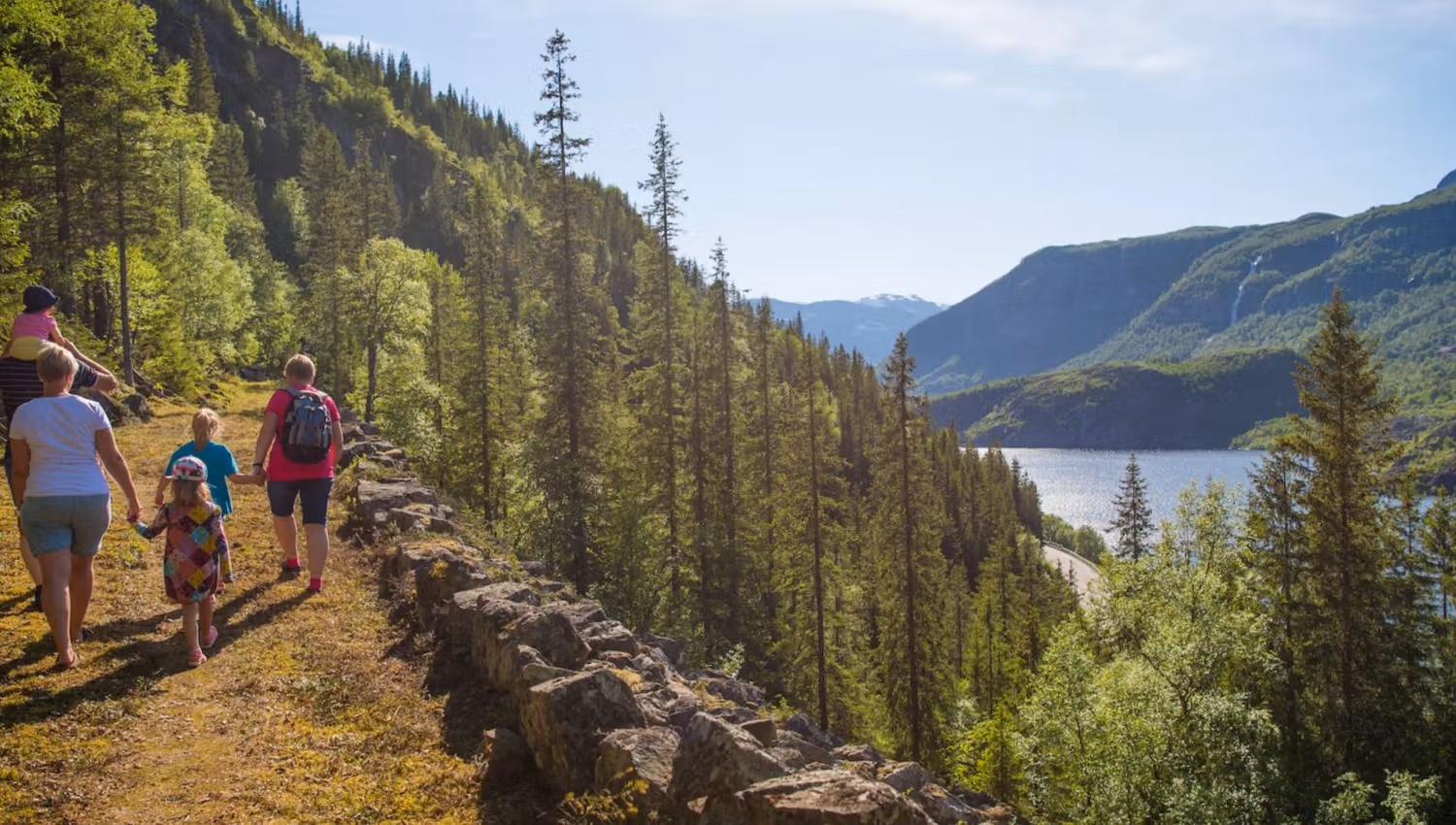 A familiy walks along a historical grass-overgrown road in a steep hillside along a lake.
