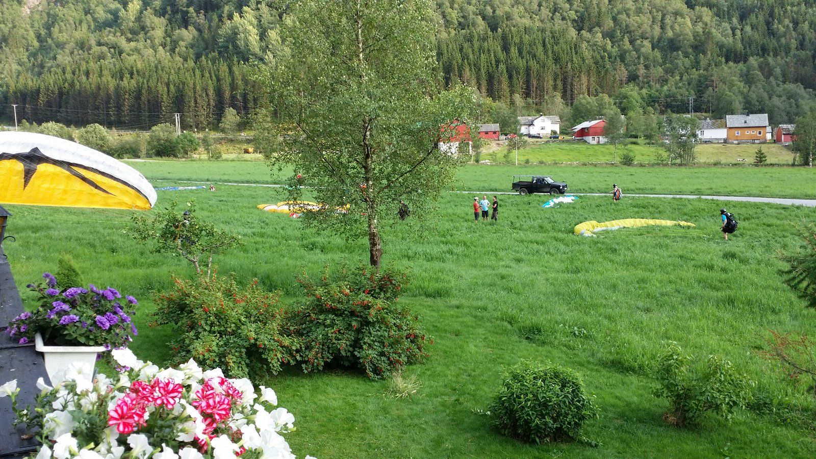 Paragliders landing near Folgefonn Farm Camping, surrounded by green meadows and mountains in Hardanger.