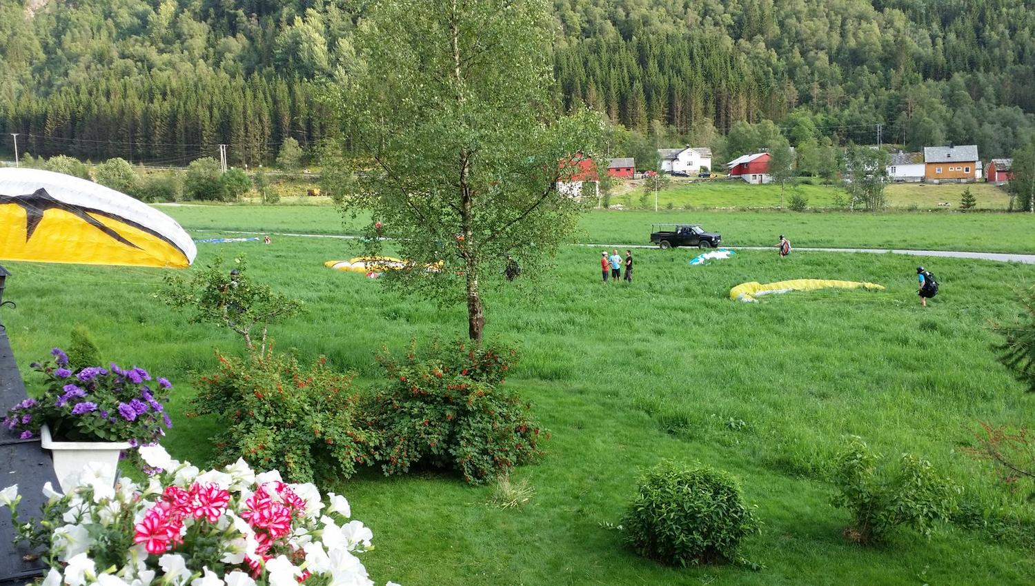 Paragliders landing near Folgefonn Farm Camping, surrounded by green meadows and mountains in Hardanger.