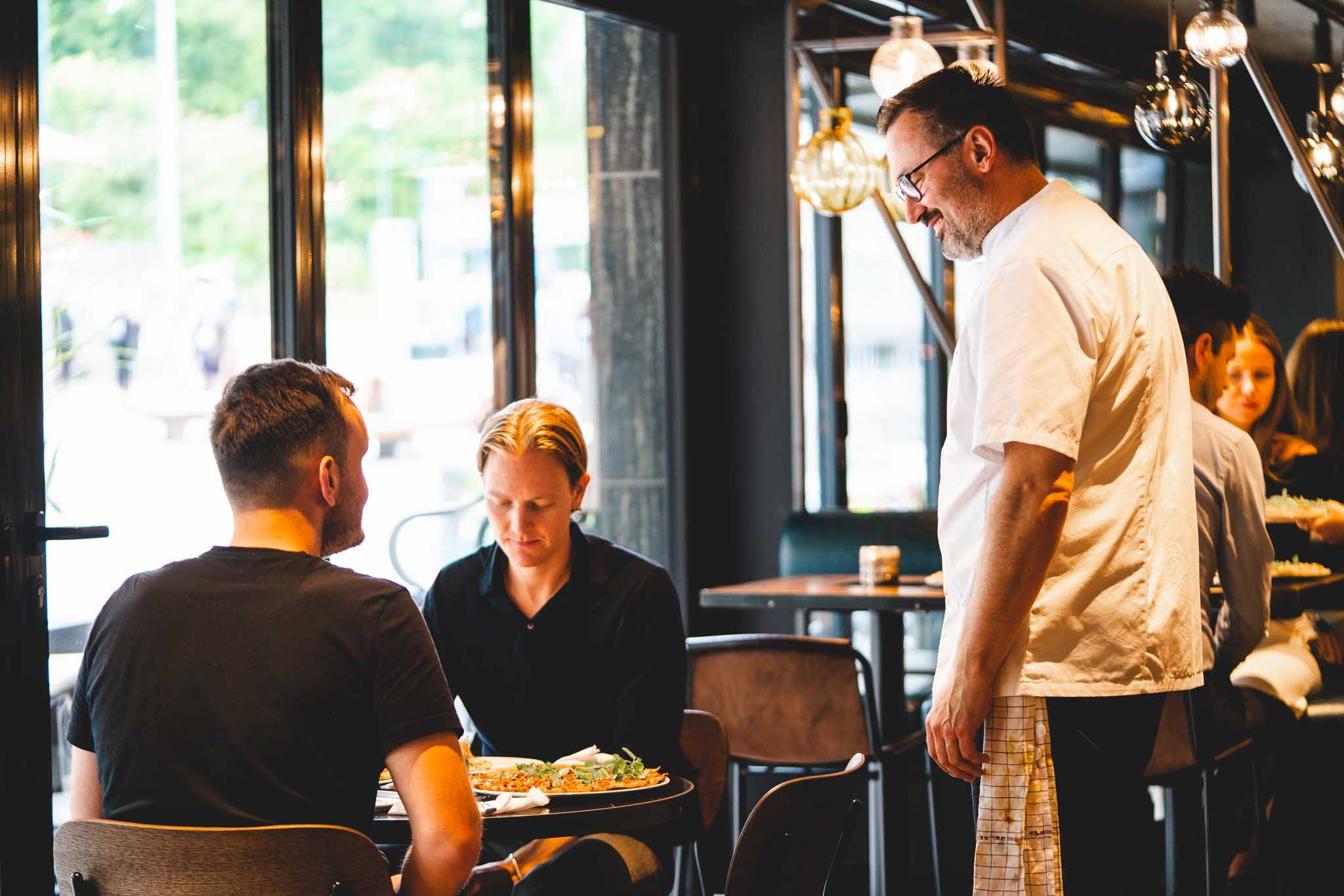 Two people sitting down at a table, a waiter stands by their table