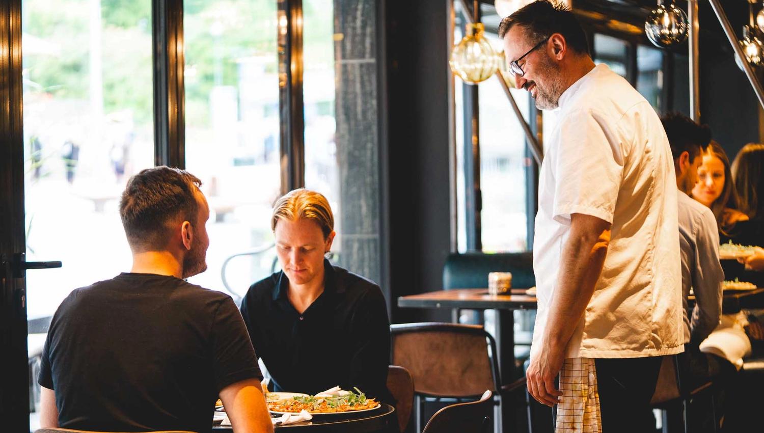 Two people sitting down at a table, a waiter stands by their table