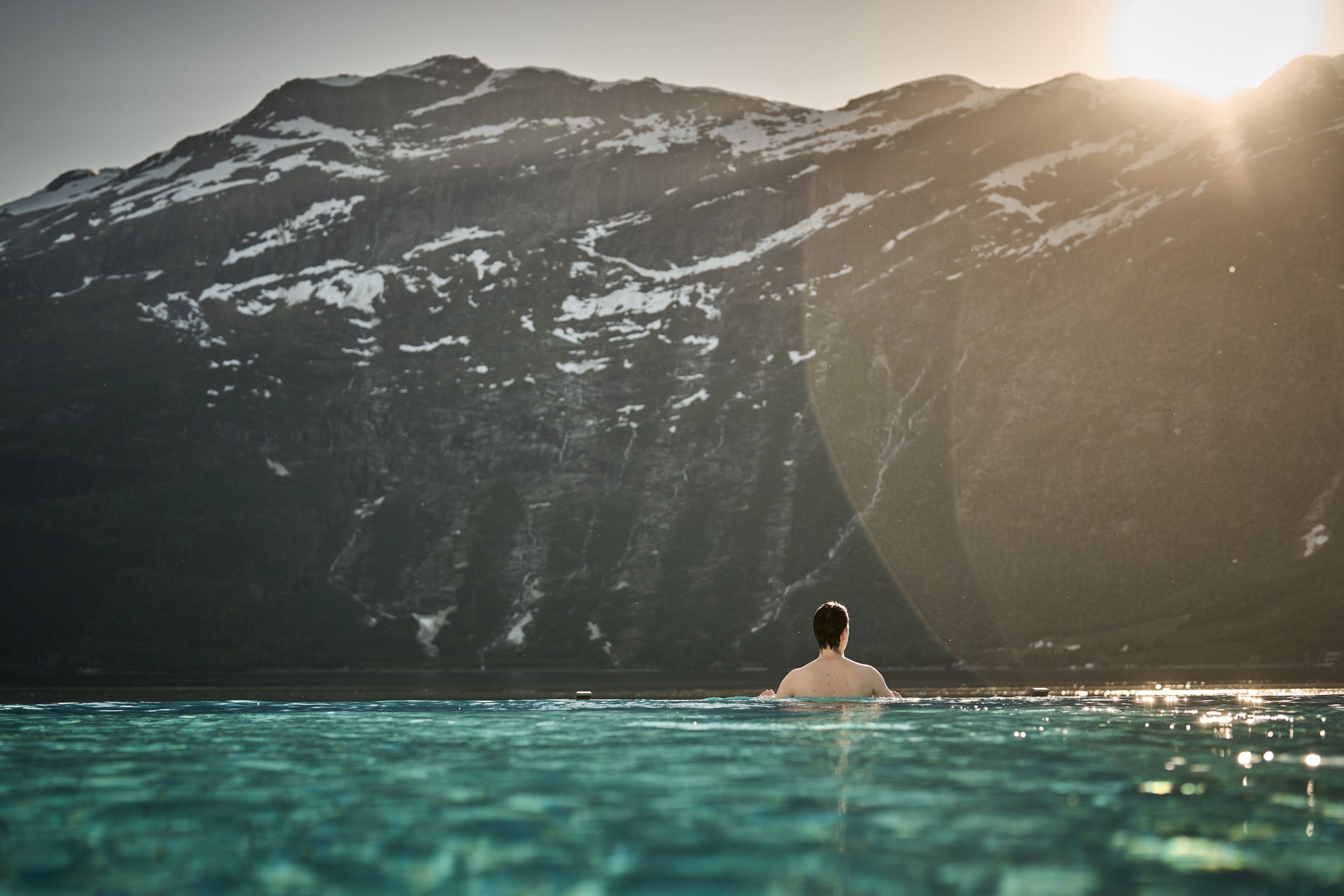 A guest enjoying the calm of evening in the infinity pool as the sun sets behind the mountains.