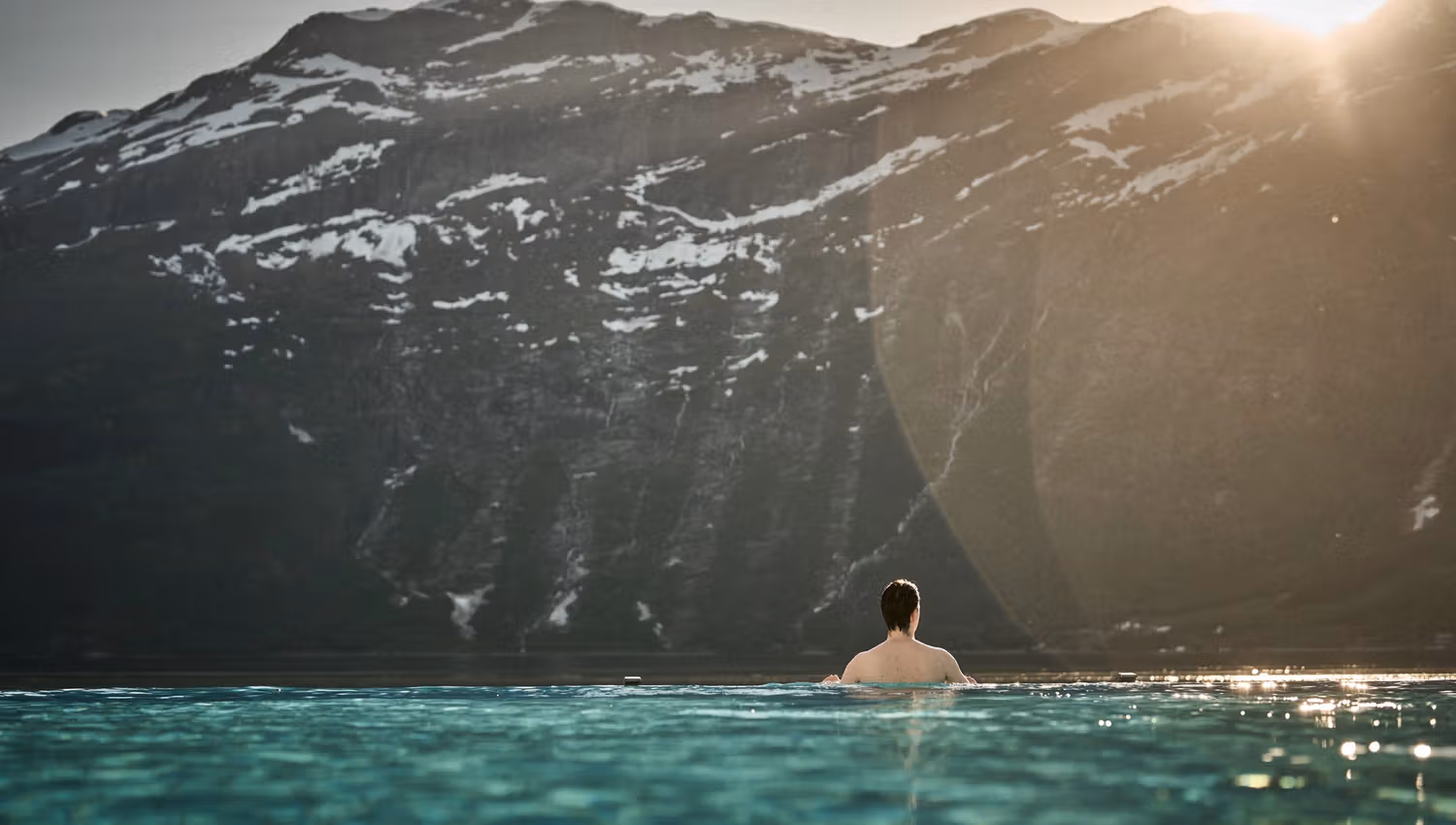 A guest enjoying the calm of evening in the infinity pool as the sun sets behind the mountains.