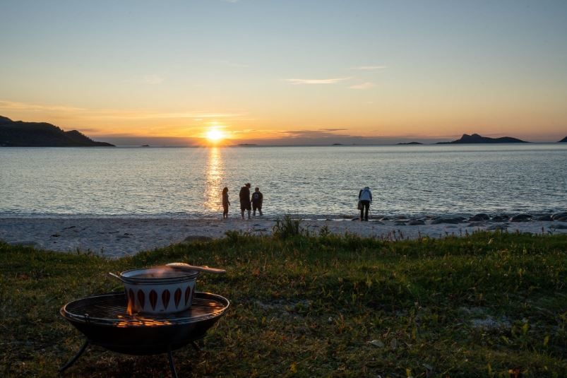 Bonfire by the shoreline with guests watching the sunset