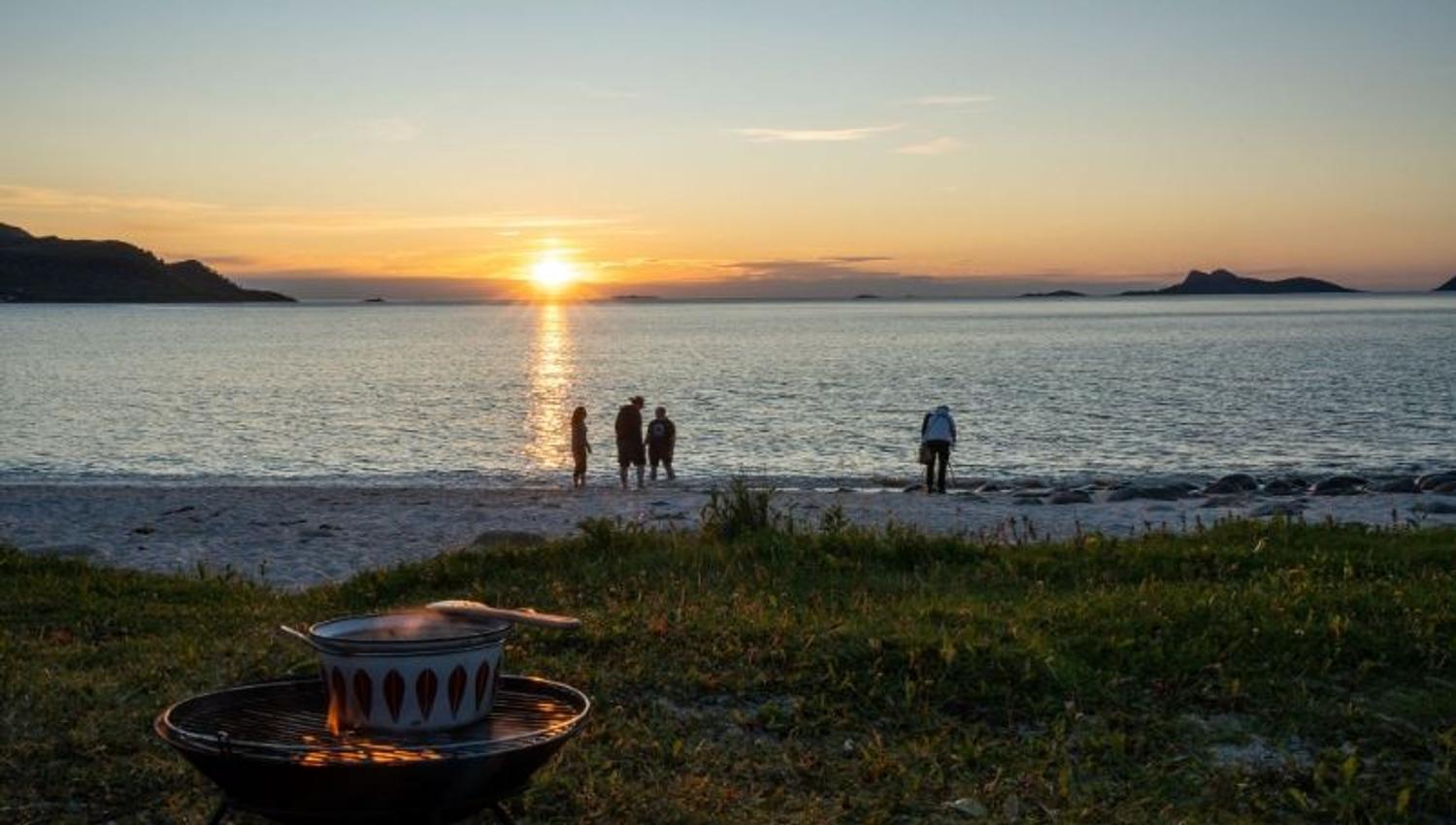 Bonfire by the shoreline with guests watching the sunset