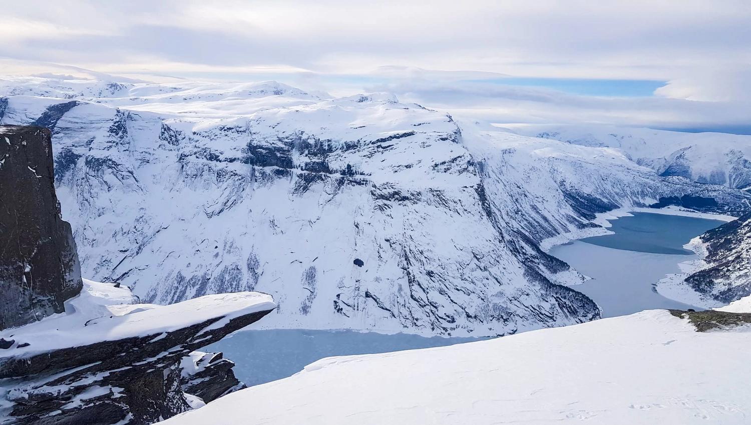 Winter landscape of Trolltunga with snow-covered mountains and a frozen fjord.