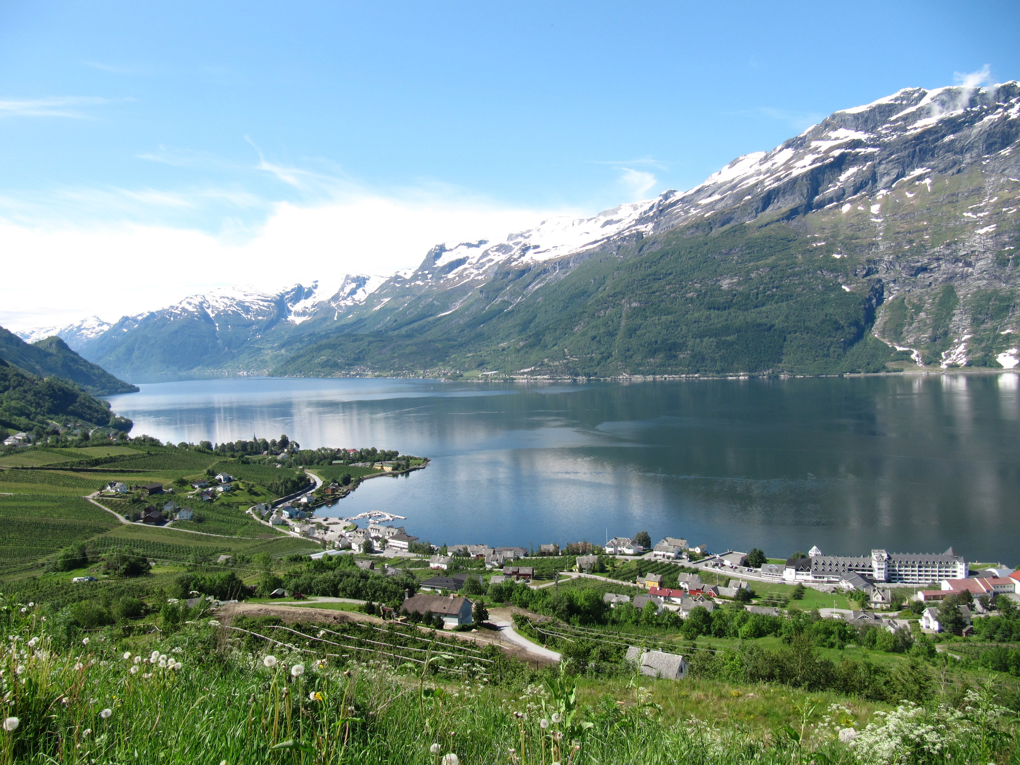 Panoramic view of Sørfjorden and the fruit farming villages in Hardanger, framed by snow-capped mountains and shimmering water.