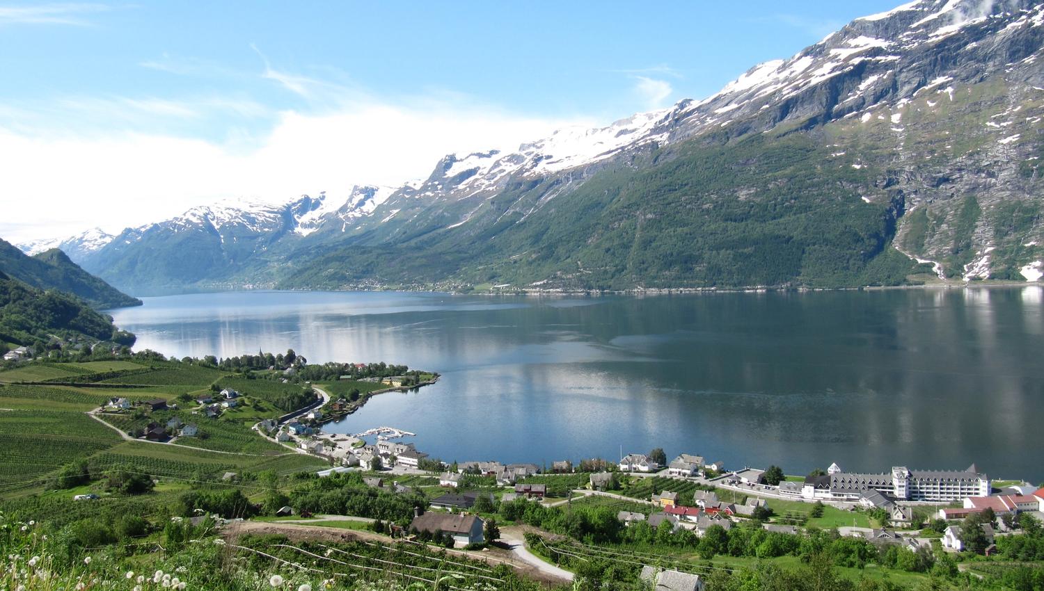 Panoramic view of Sørfjorden and the fruit farming villages in Hardanger, framed by snow-capped mountains and shimmering water.