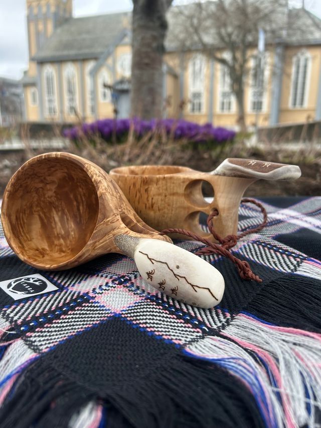 Traditional Sámi guksis (wooden cups) displayed on a patterned shawl, with Tromsø Cathedral in the background.
