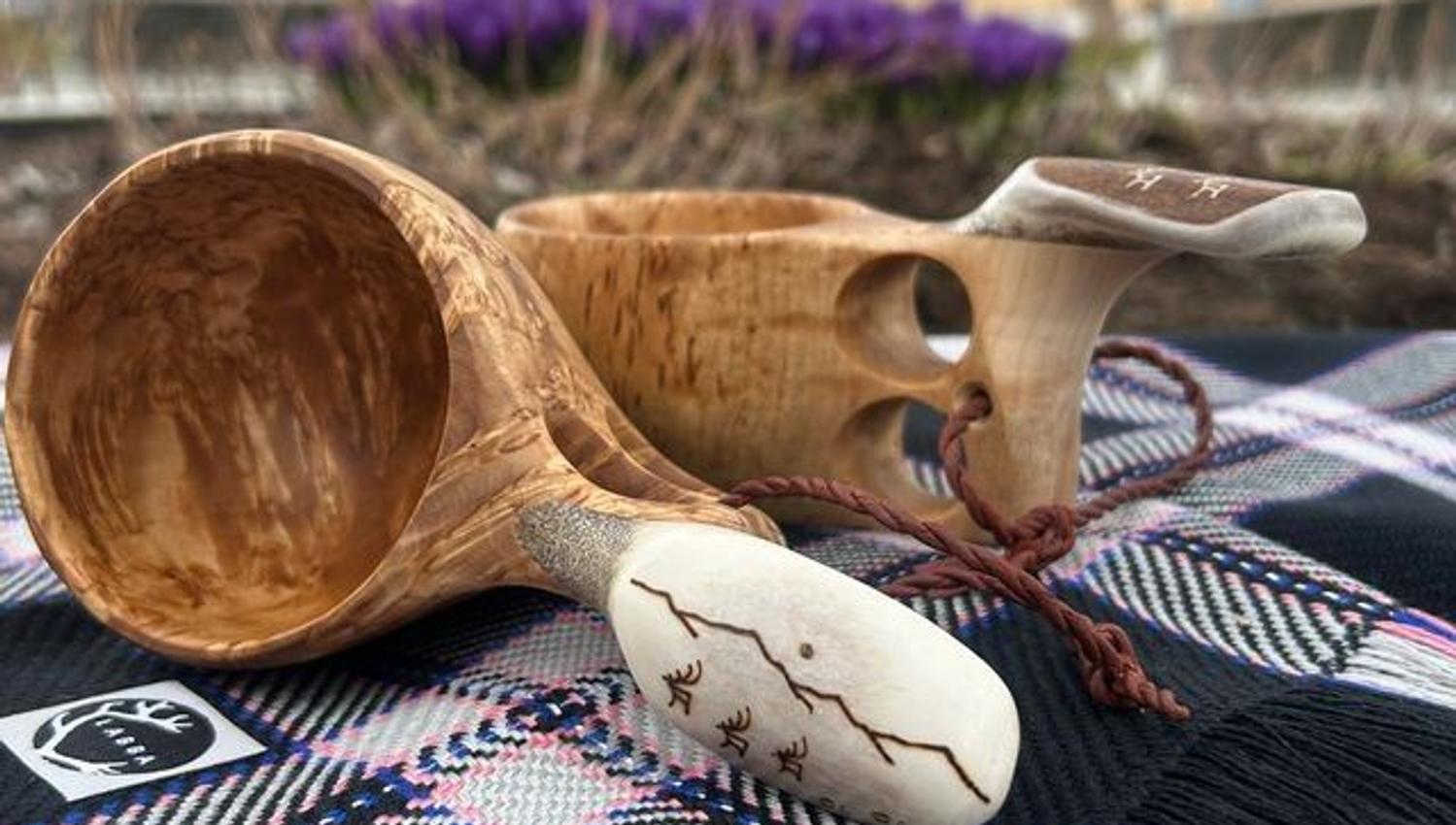 Traditional Sámi guksis (wooden cups) displayed on a patterned shawl, with Tromsø Cathedral in the background.