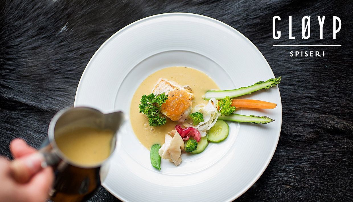 An elegant dish served at Gløyp Spiseri featuring fresh vegetables and fish, with sauce being poured over.