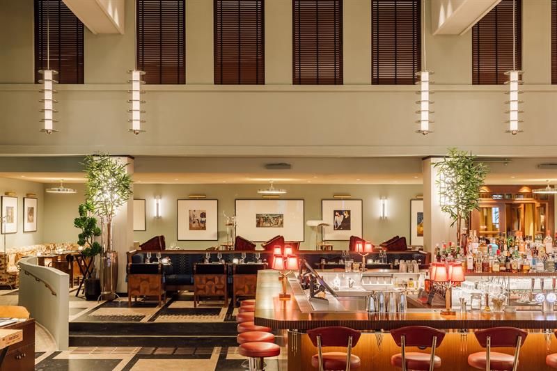 Spacious hotel bar with high ceilings, stylish bar stools, soft lighting, and elegant seating areas in warm tones.
