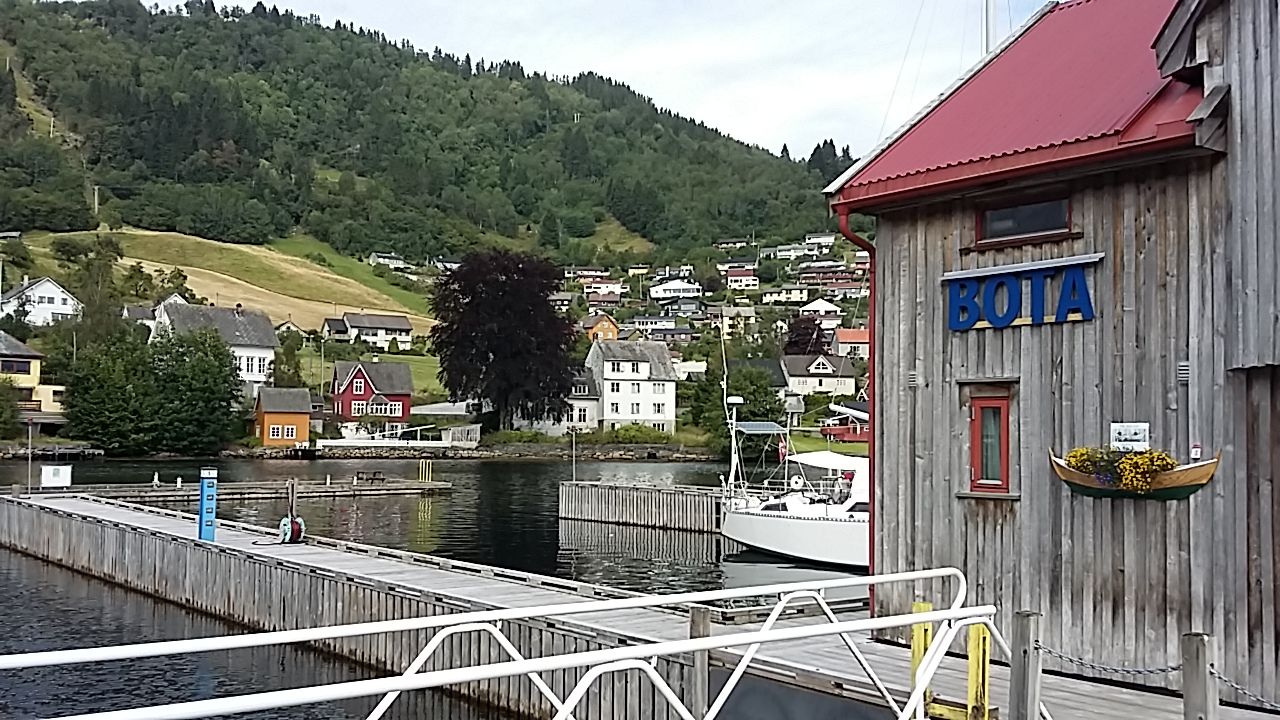 Wooden boathouses with red roofs at Norheimsund Guest Harbour, with boats and scenic fjord views.