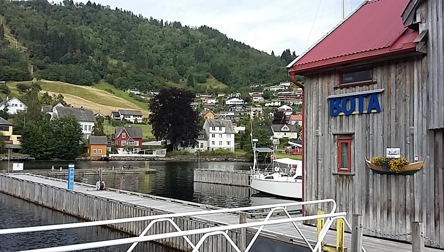 Wooden boathouses with red roofs at Norheimsund Guest Harbour, with boats and scenic fjord views.