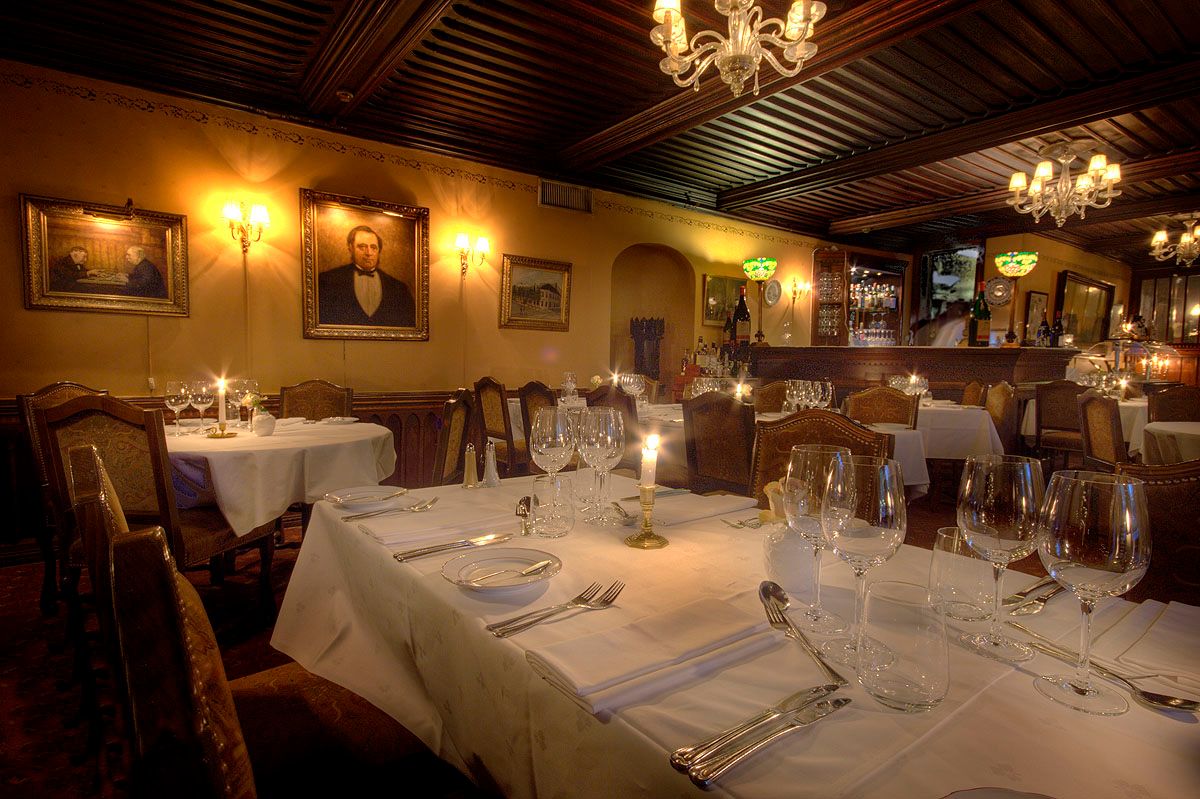 Interior with clothed tables set for dining, old paintings on the yellow walls.