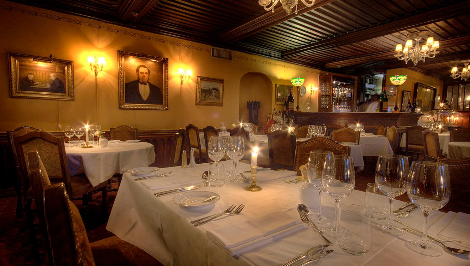 Interior with clothed tables set for dining, old paintings on the yellow walls.
