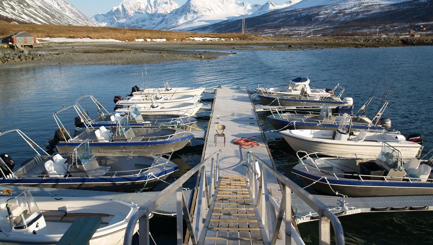Jetty with small boats, a ramp, and a view of snow-covered mountains under a blue sky