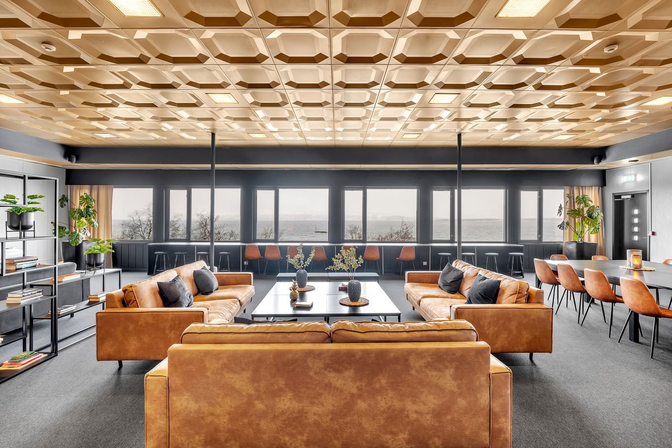 Moderne lounge med skinnsofaer, store vinduer og dekorative detaljer.