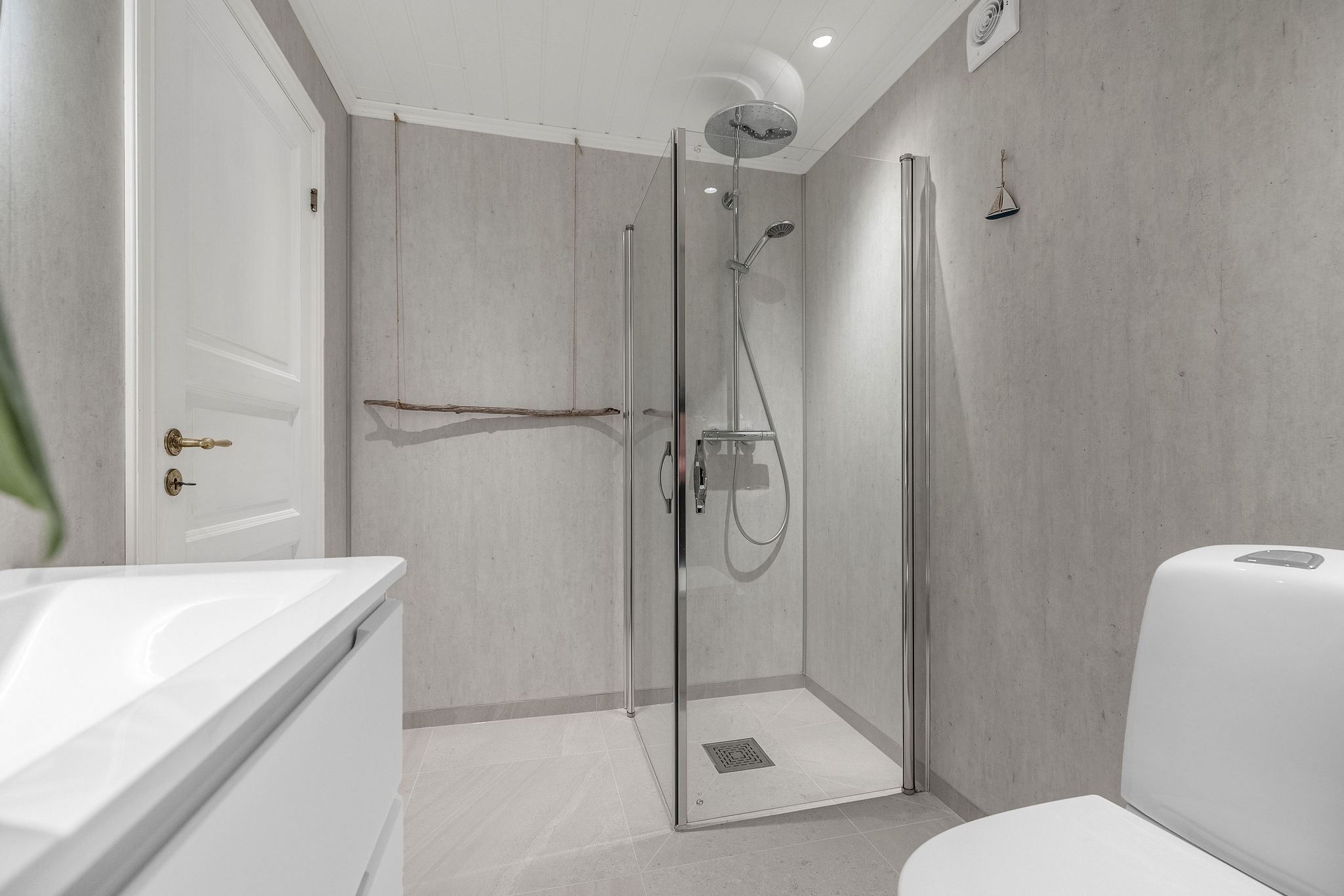 Modern gray bathroom with glass shower enclosure, rainfall showerhead, white vanity, and toilet under recessed lights at the Seahouse at Hornelen Panorama in Bremanger..