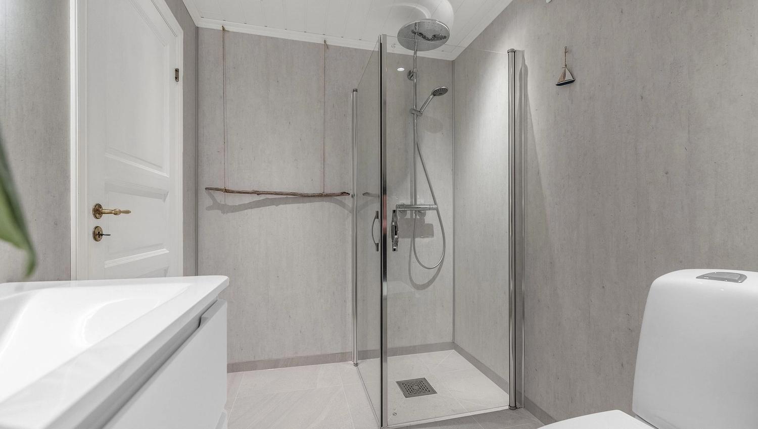 Modern gray bathroom with glass shower enclosure, rainfall showerhead, white vanity, and toilet under recessed lights at the Seahouse at Hornelen Panorama in Bremanger..