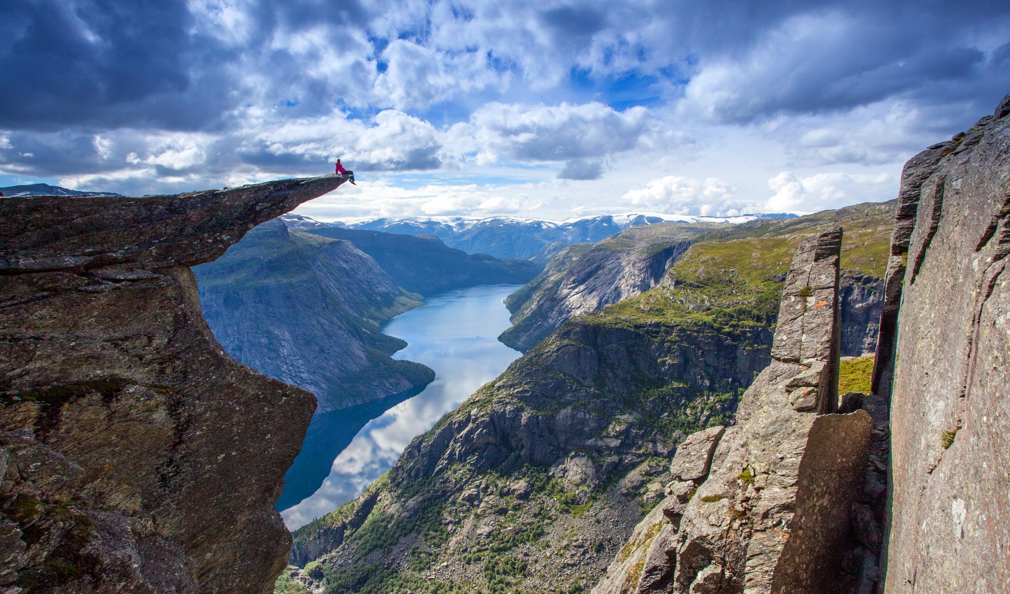 Person sitting on Trolltunga cliff with dramatic fjord and mountain landscape in Hardangervidda, Hardanger.