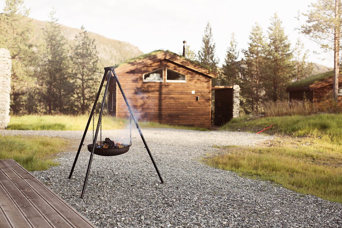 Une cheminée en plein air avec de la fumée, près d'un chalet en bois entouré par la nature.