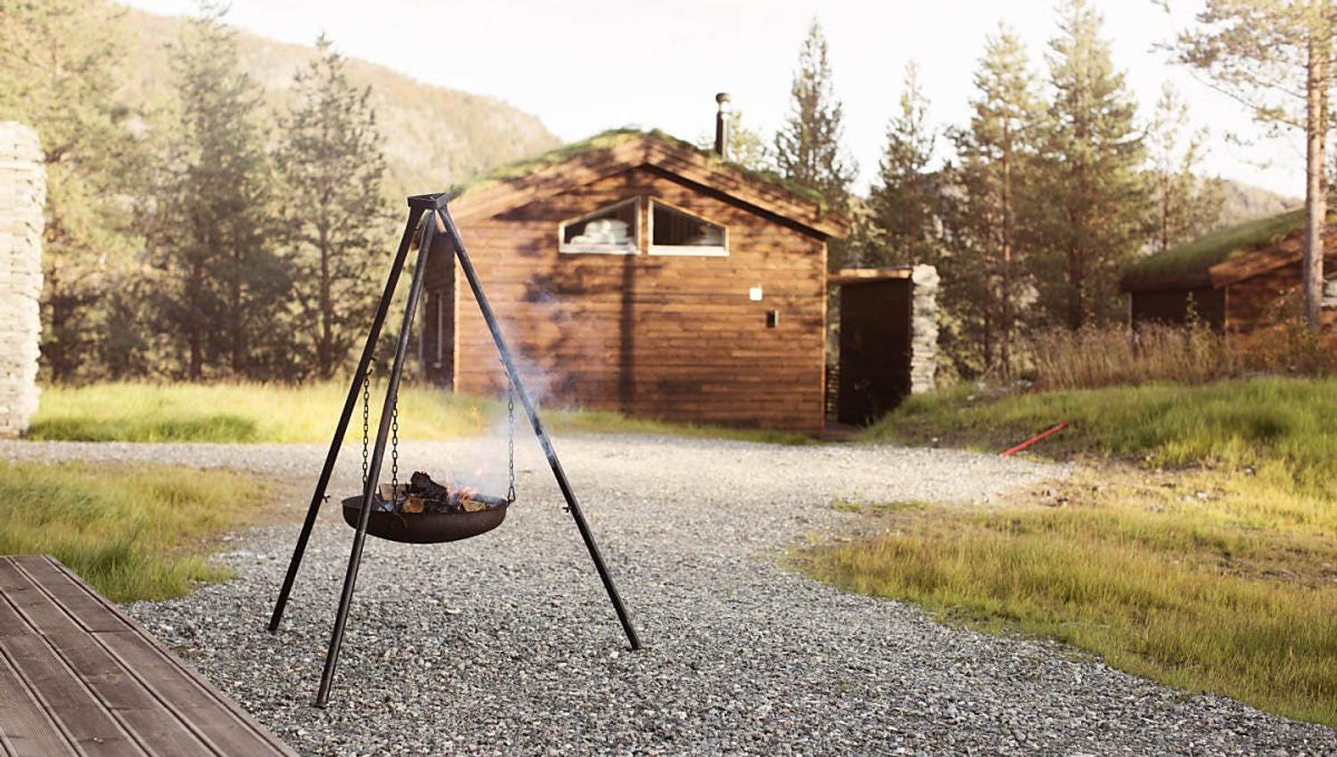 Une cheminée en plein air avec de la fumée, près d'un chalet en bois entouré par la nature.