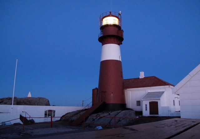 Ryvingen Lighthouse with the light on in the lantern room in the evening.
