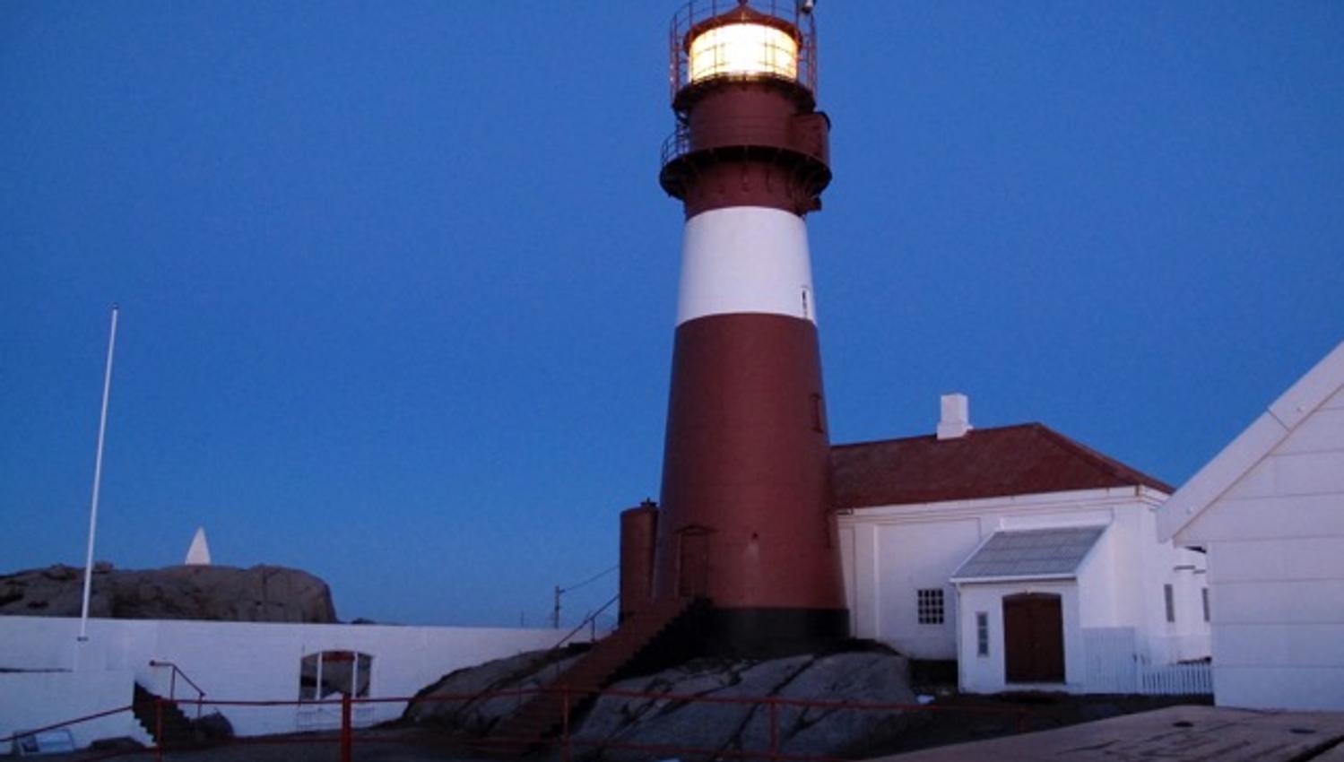 Ryvingen Lighthouse with the light on in the lantern room in the evening.