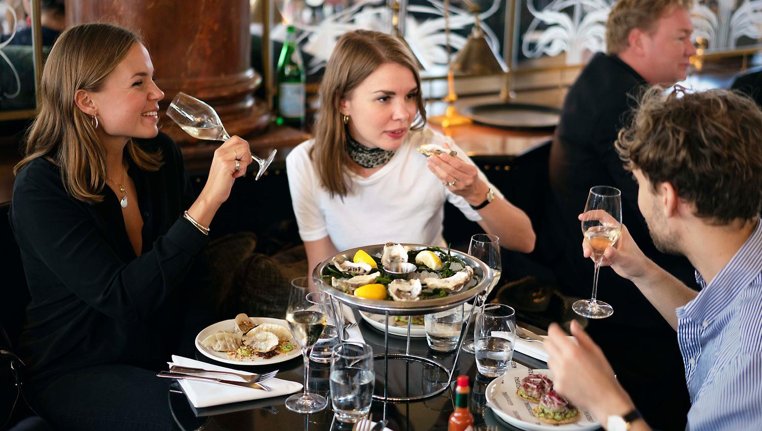 Three people drinking white wine and eating seafood.