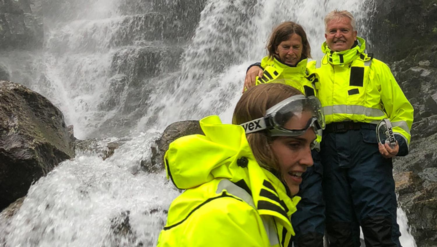 Excited participants stand close to the waterfall, feeling the powerful spray on a RIB safari in Hardanger.