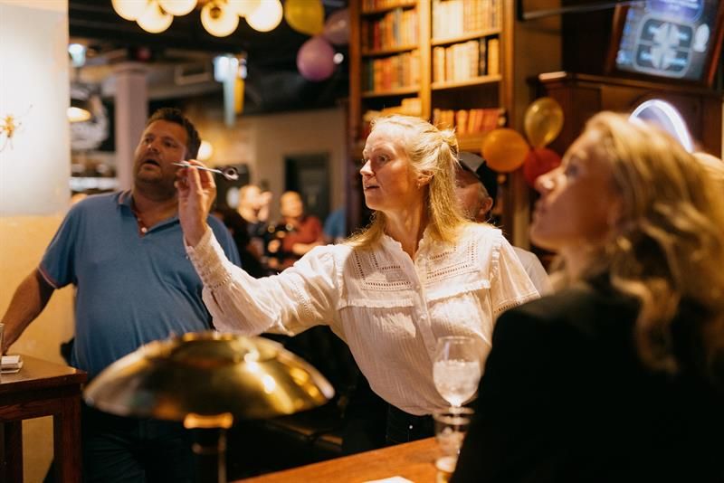 Dame som er i ferd med å kaste en dartpil mens noen andre mennesker ser på