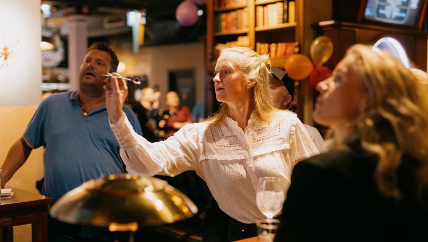 Dame som er i ferd med å kaste en dartpil mens noen andre mennesker ser på