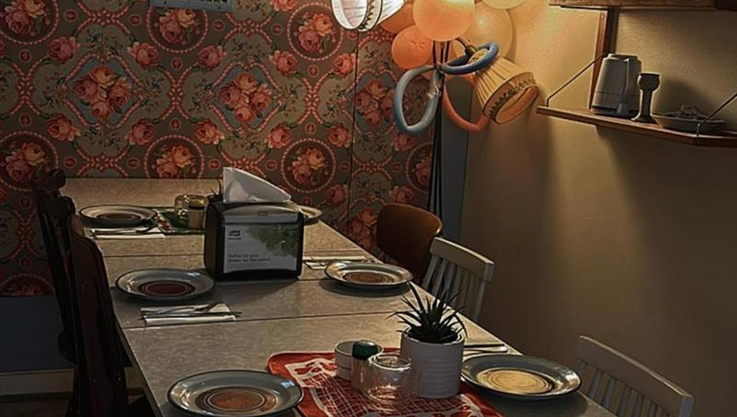 Oppdekket bord med tallerkener, glass og blomster i et kafélokale med mønstret tapet hos Nummer Ti i Horten.