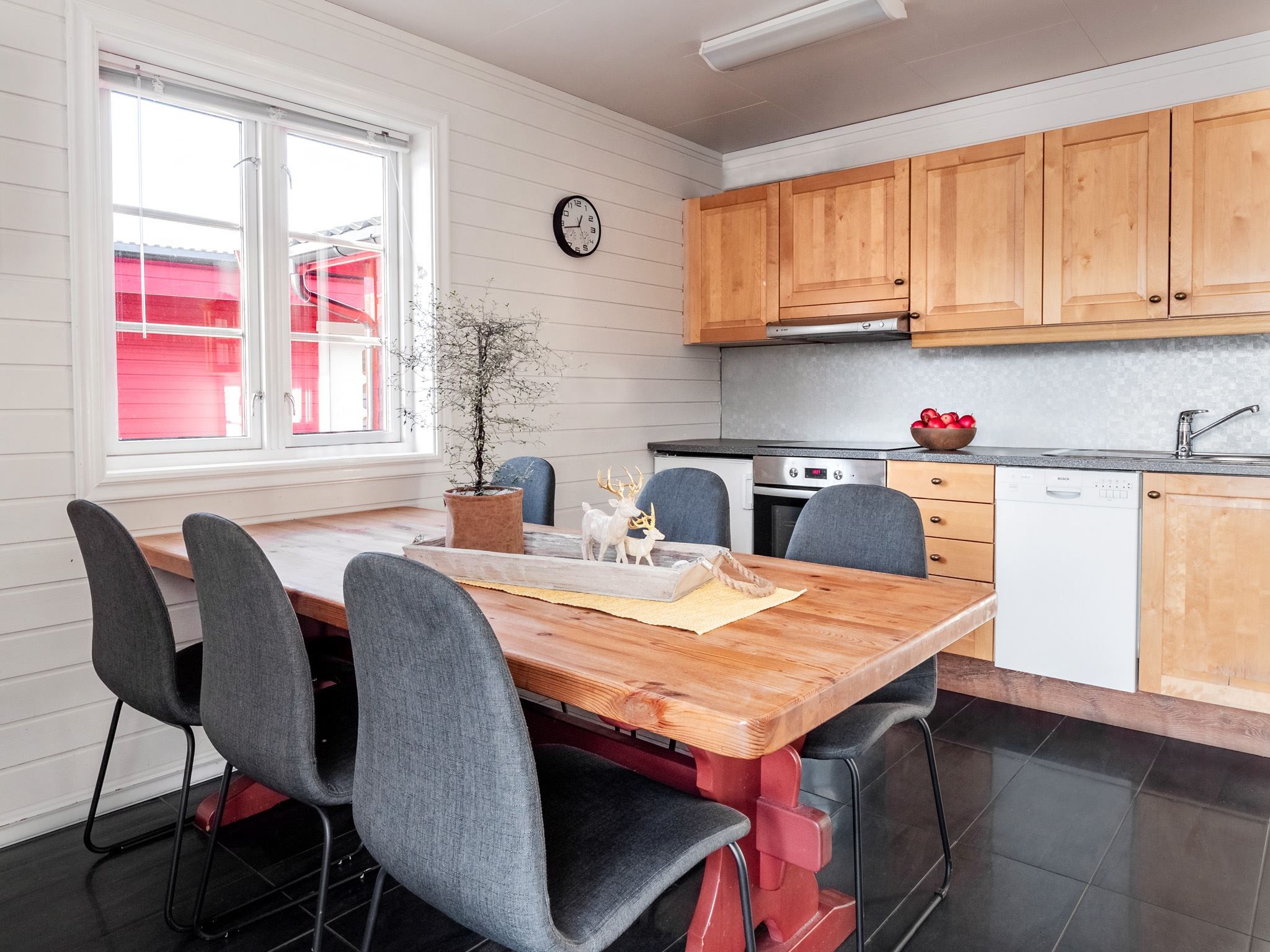 Modern kitchen and dining area with a wooden table, grey chairs, and decorations featuring a reindeer figure and plants