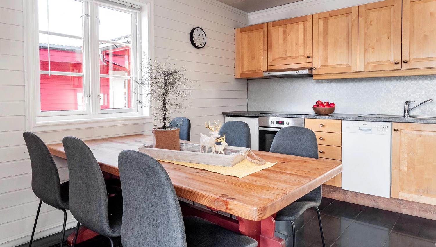 Modern kitchen and dining area with a wooden table, grey chairs, and decorations featuring a reindeer figure and plants