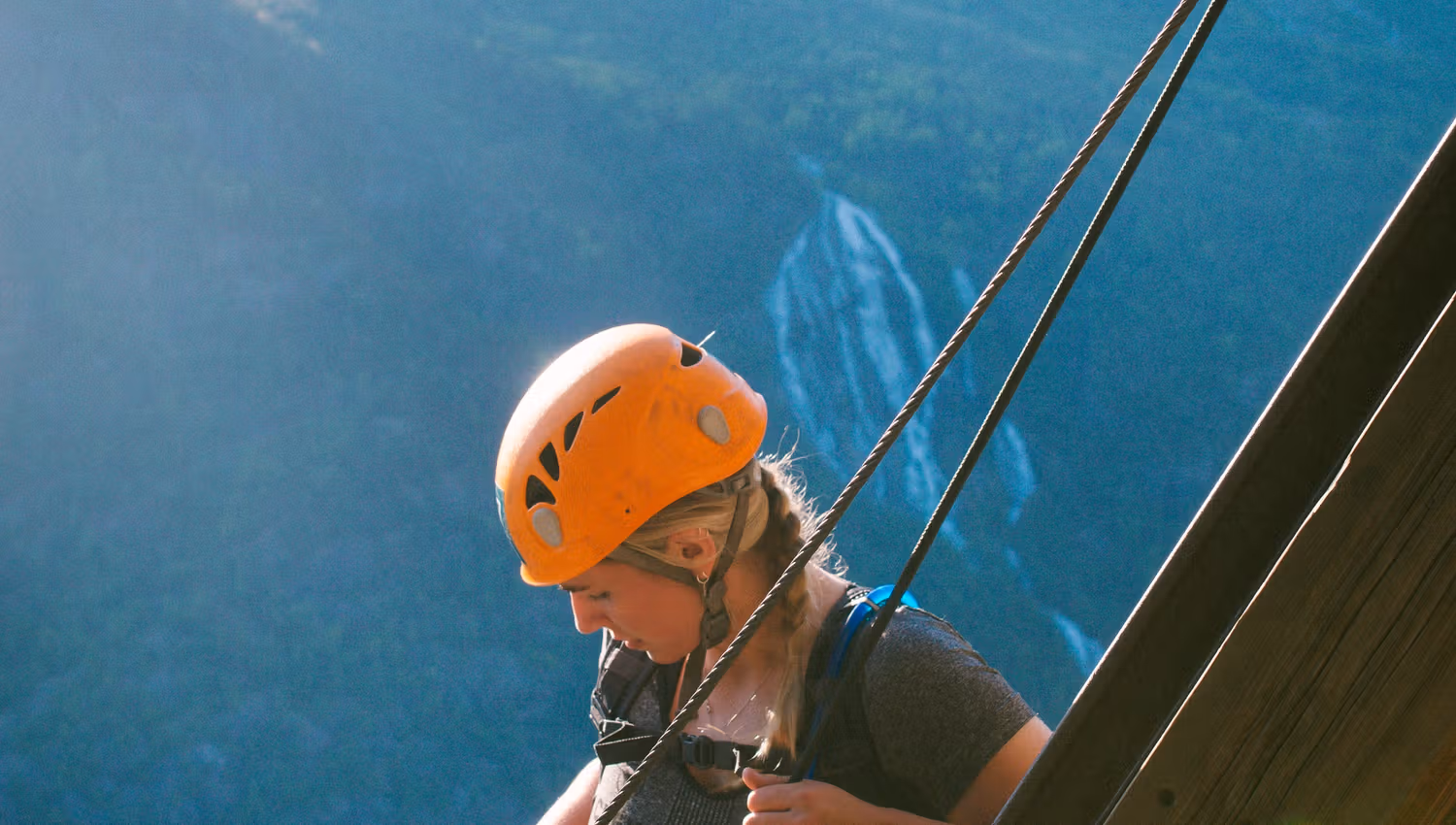 Climber secured to the steel cable with waterfall and mountains in the background.
