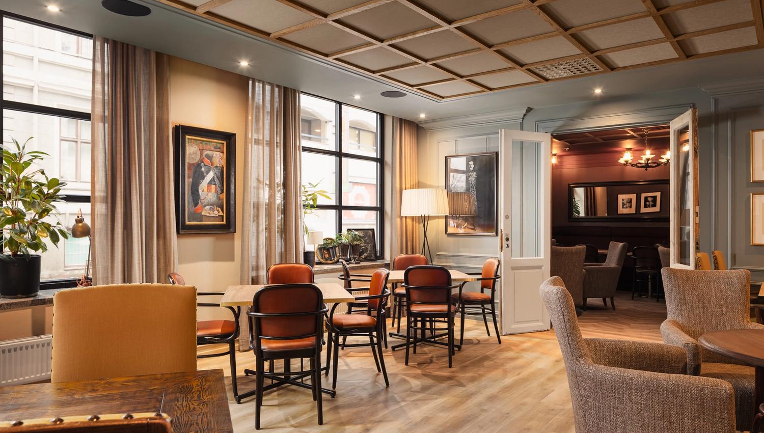 A chambre séparée with small tables and orange chairs, large windows, and armchairs