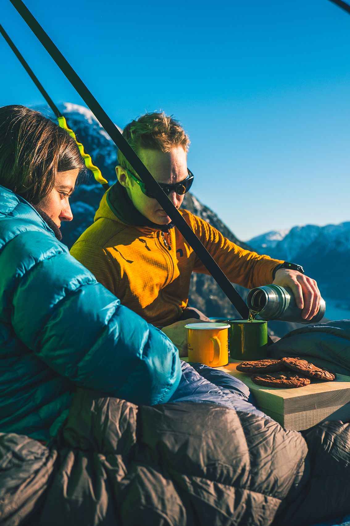 Eit par nyt kaffi og kjeks i solskinet medan dei heng på ein portaledge i fjellveggen over Hardangerfjorden. Uforgløymeleg oppleving i naturen.