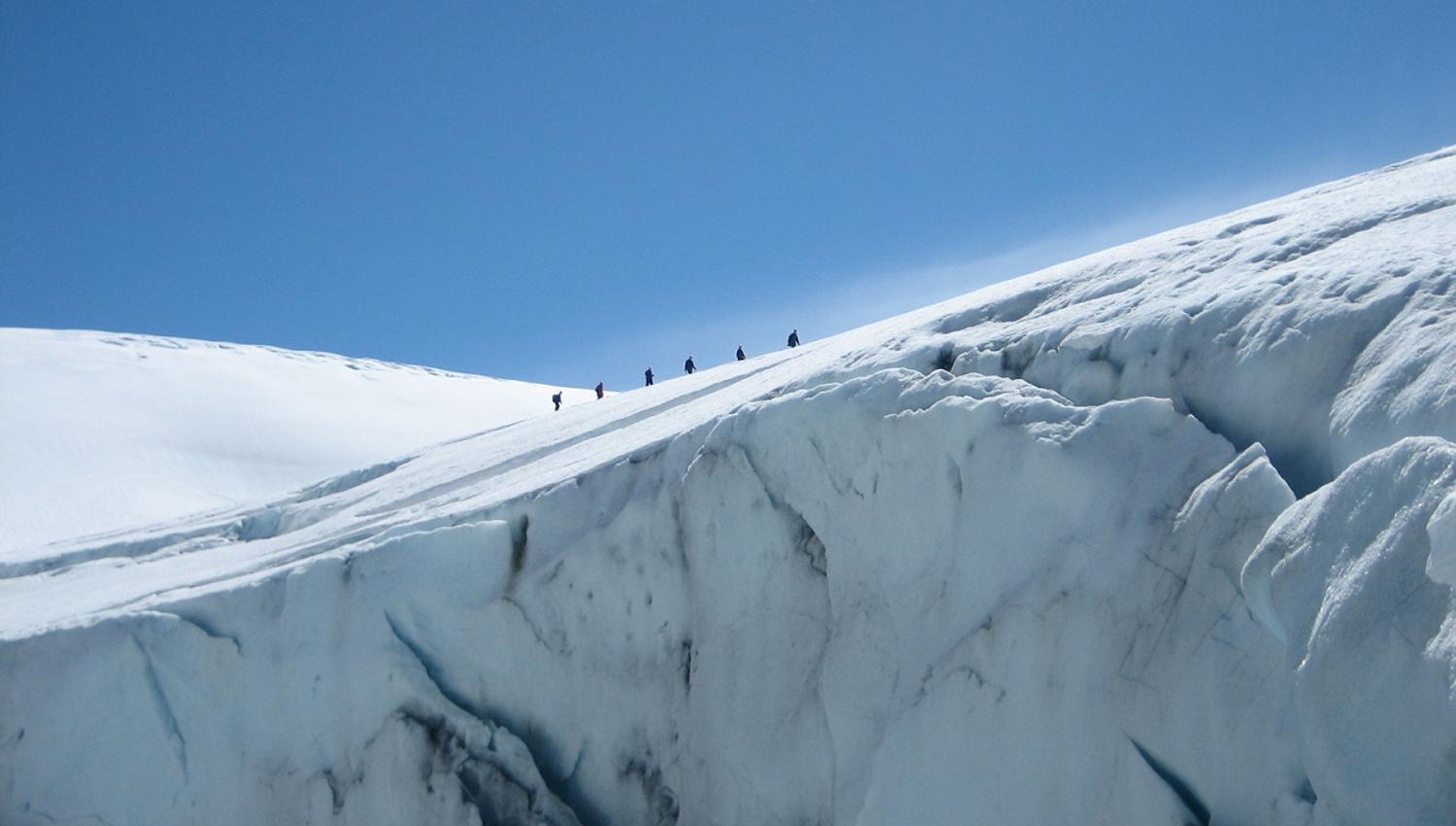 Small groups of hikers move along the top of the Folgefonna Glacier with majestic ice crevasses beneath them.