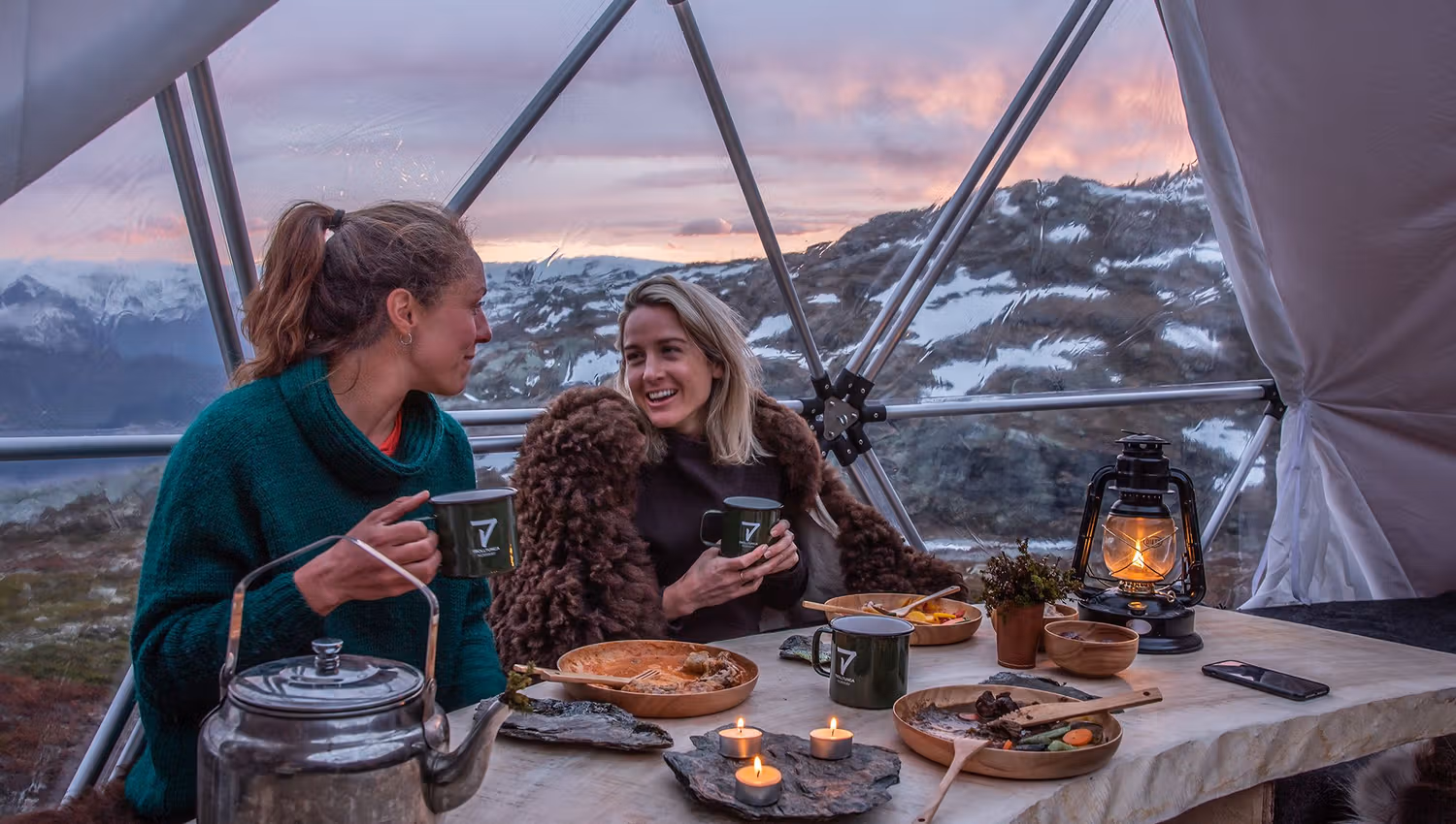 Two guests enjoying warm food and candlelight inside the glamping dome near Trolltunga.