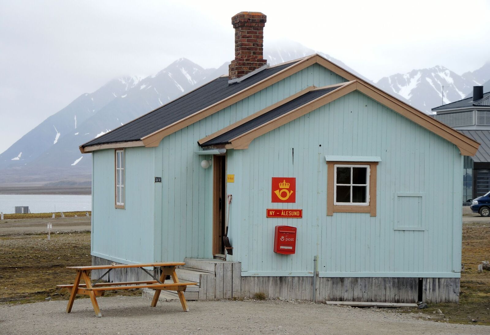 A blue building in Ny-Ålesund known as the post office, seen from the outside with mountains in the background