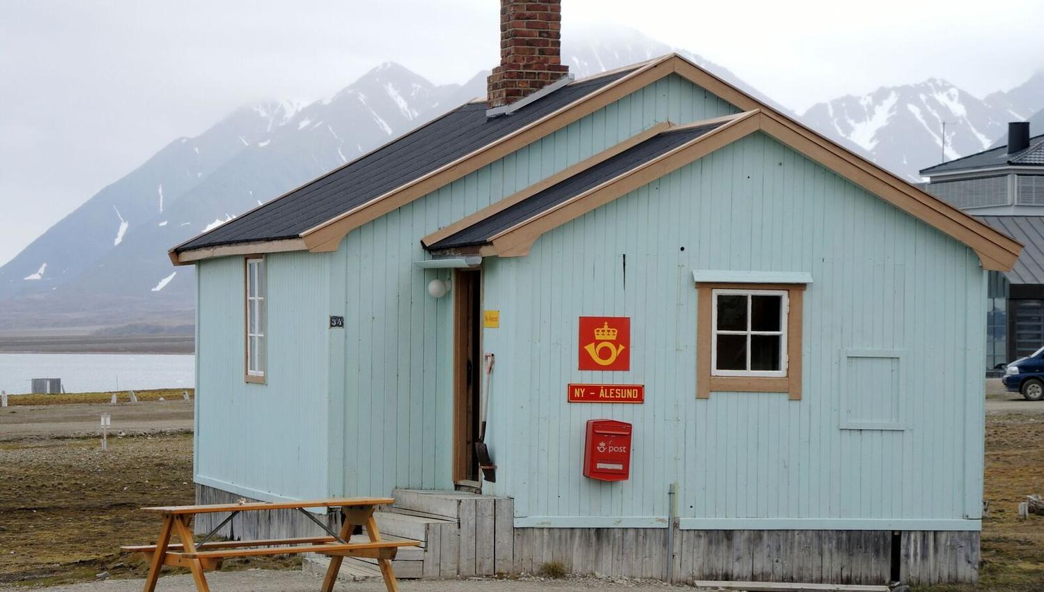 A blue building in Ny-Ålesund known as the post office, seen from the outside with mountains in the background