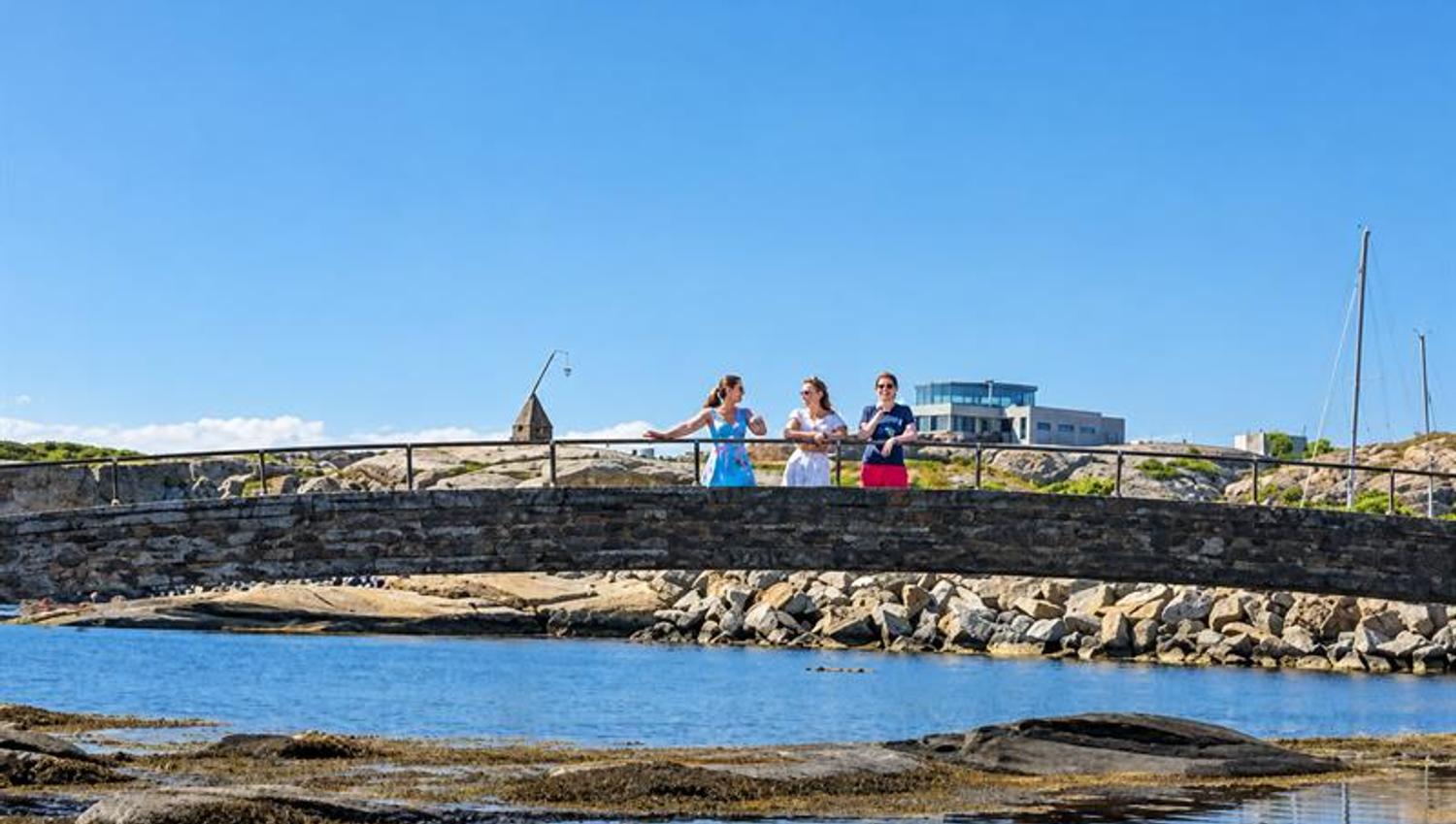 Three people standing on a low stone bridge over the water at Verdens Ende on Tjøme.