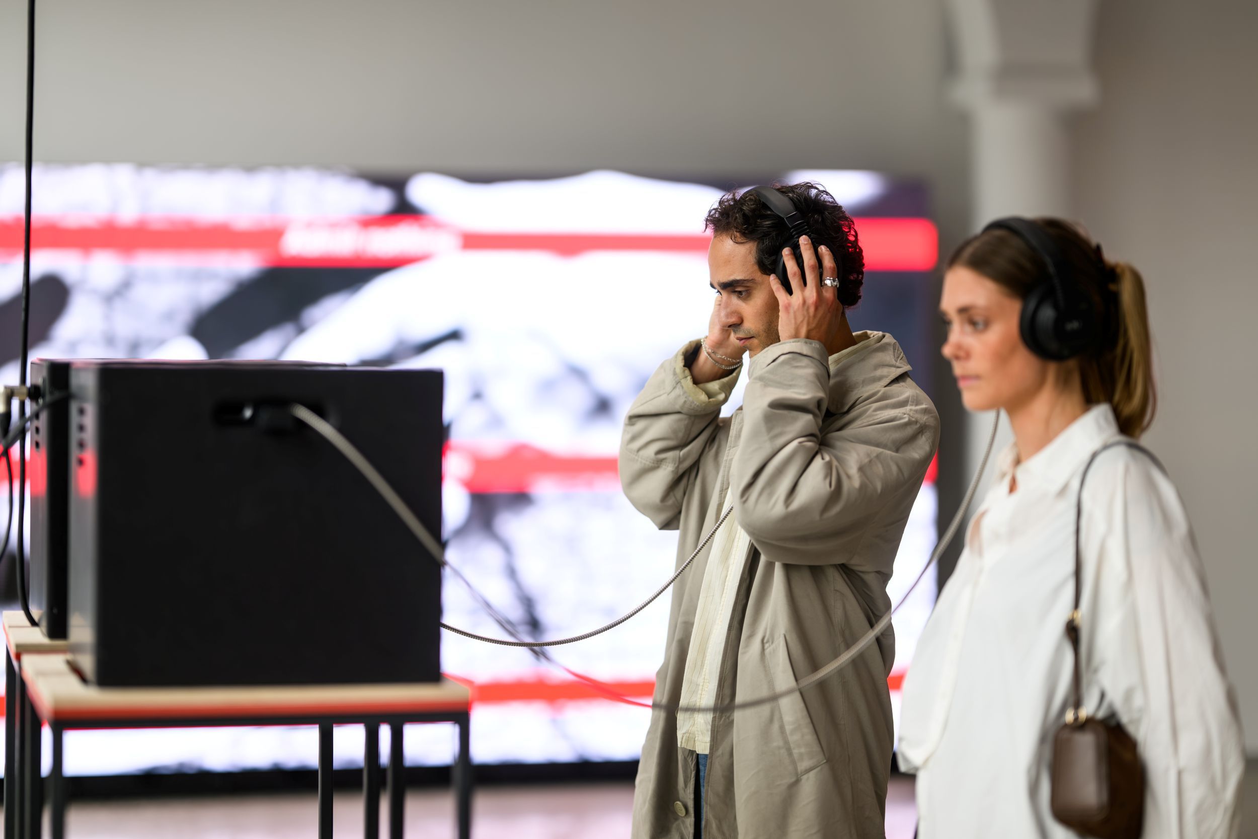Two people wearing headphones experience a sound installation at the Nobel Peace Center. A man in a light coat stands focused in front of the equipmen