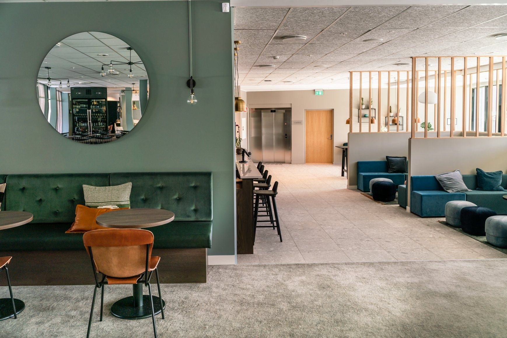 Modern café area with green seating and a round mirror on the wall.